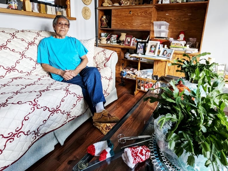 A woman in a blue shirt and jeans sits on a couch in a living room. 