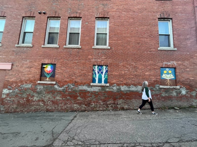 Murals on a brick wall include a rainbow around a flower, and trees, and dandelions.