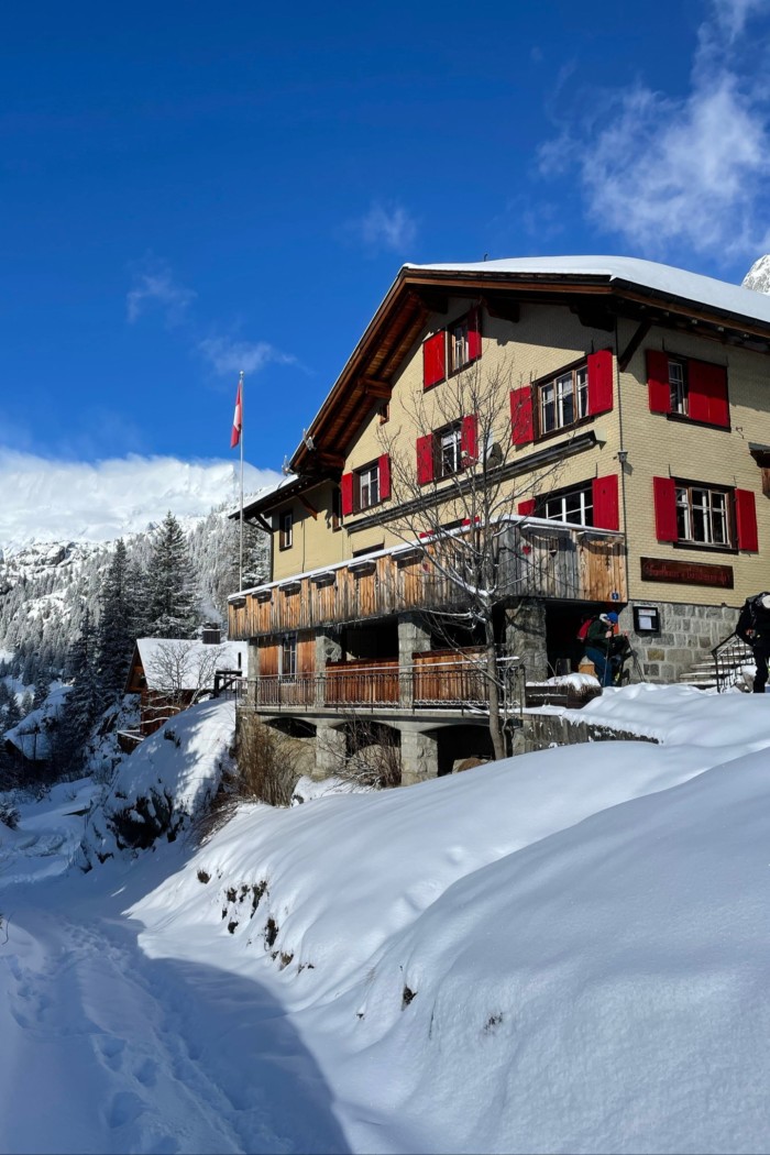 A classic Swiss chalet with red shutters on a snowy mountainside under blue skies