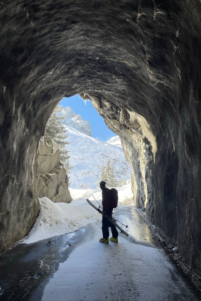 A single skier inside the small tunnel and silhouetted against the blue sky beyond