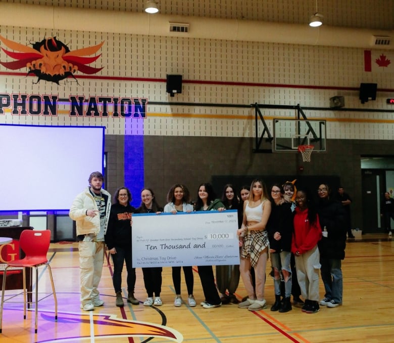 A group of people pose in a school gymnasium holding a prop cheque for $10,000.