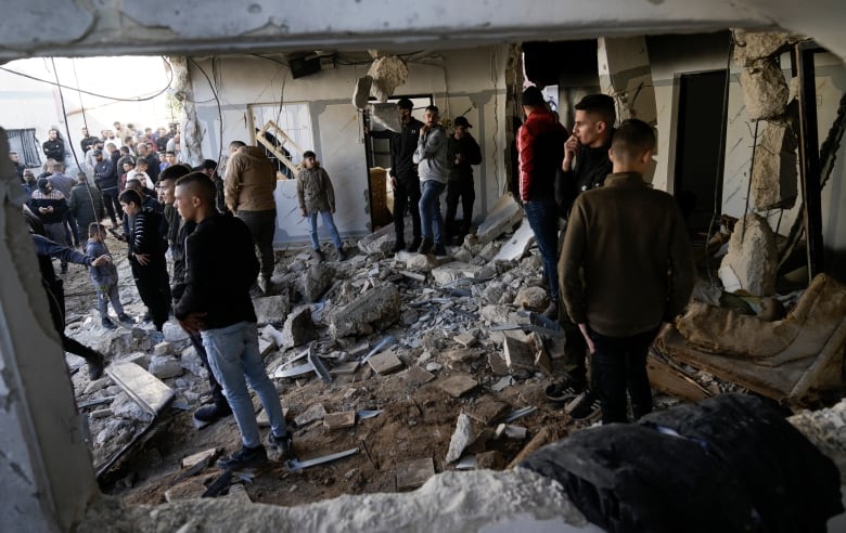 A group of people stand amid rubble after a building was demolished.