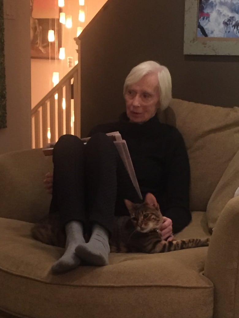 A woman curled up with a cat on a couch looks off camera with a look of wonderment on her face.  