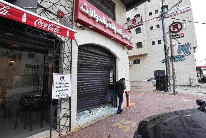 A Palestinian man inspects damage to a money exchange shop after a raid by the Israeli army