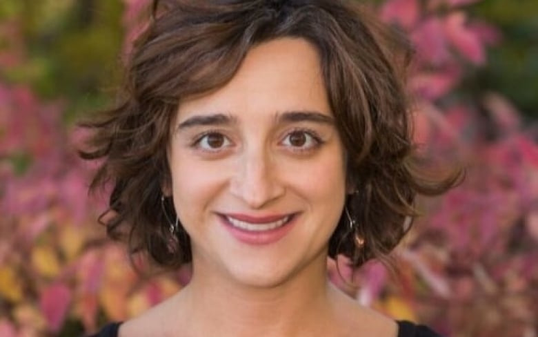 Dr. Cora Constantinescu smiles as she looks directly into the camera. Colourful foliage can be seen behind her.