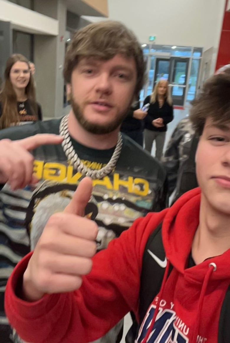 A teen takes a selfie with a man. Both hold up a finger. 