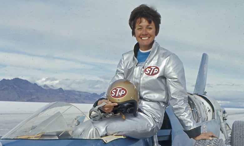 A woman sits on top a race car. 