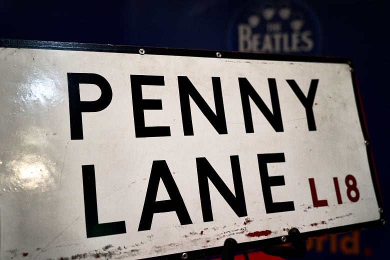 A white street sign, lightly scratched, with black text that reads: 'PENNY LANE L18"