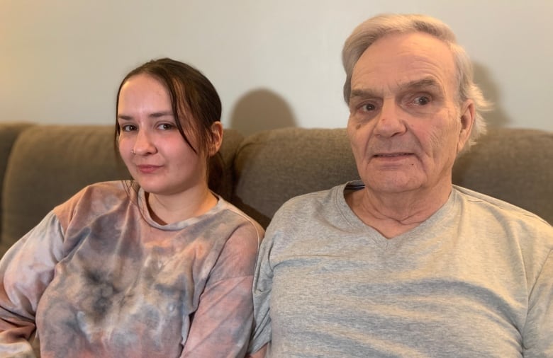 A woman and a man sit side-by-side on a beige couch.