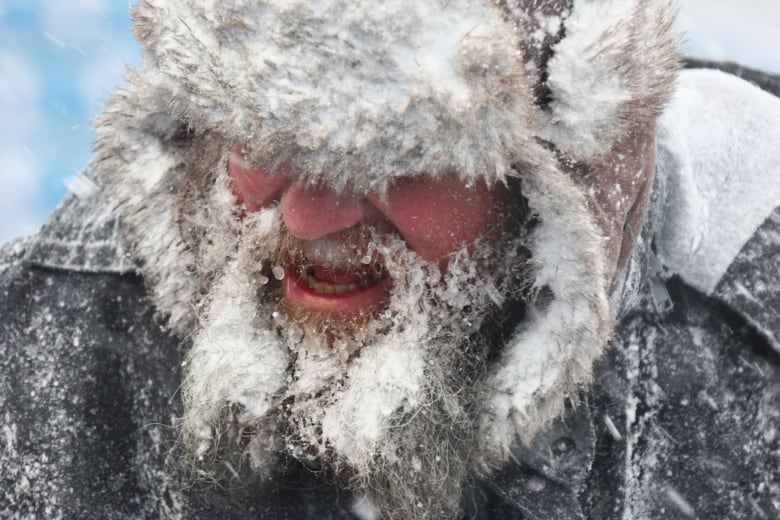 Closeup of a man's face, his beard, moustache and fur hat matted with ice and snow. 