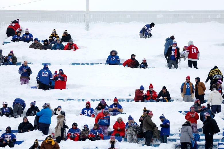 Football fans bundled in winter gear sit in snow-covered stadium seats.