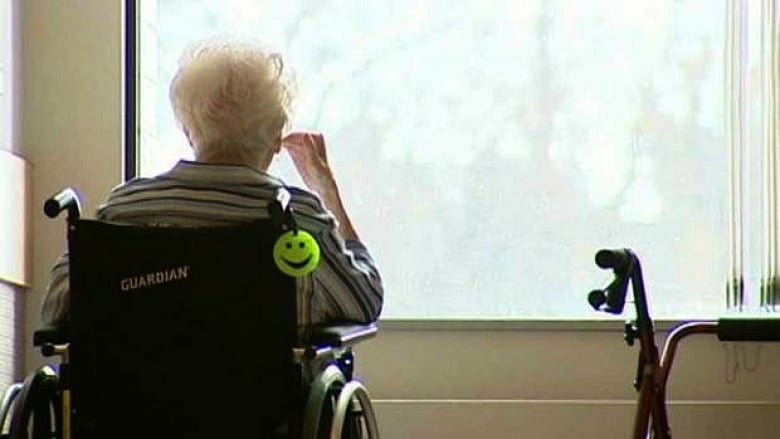 The back of an elderly woman sitting in a wheelchair, looking out a window.