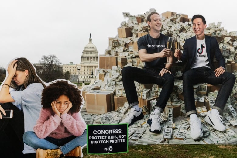 An installation depicts two people sitting on a pile of cash and toasting with champagne while children look distraught.