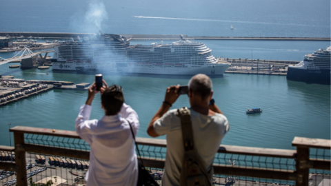 Tourists seen from behind taking pictures from the deck of their cruise ship of another cuise ship in Barcelona port