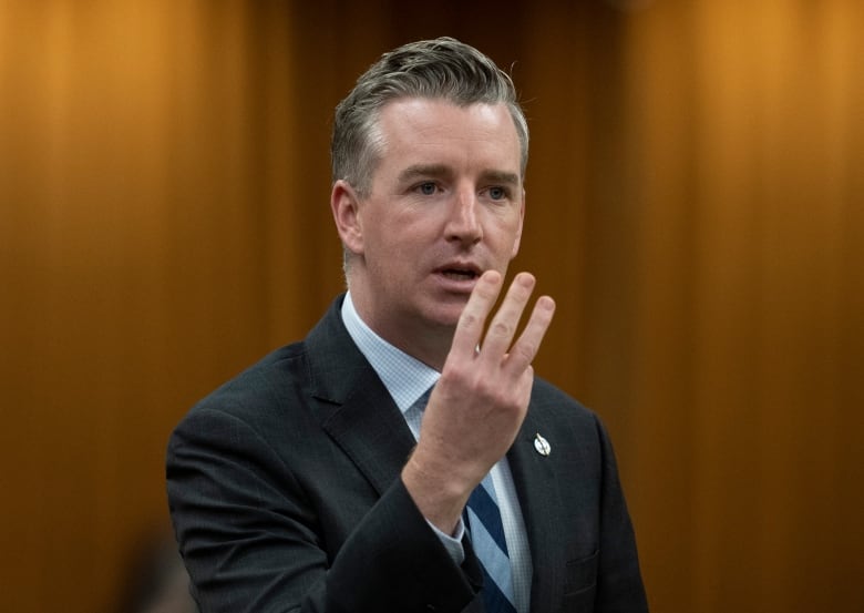 A politician holds up three fingers as he speaks in a legislature.