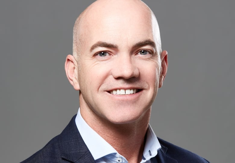 A photograph of a smiling, bald man. 