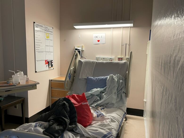 A hospital bed can be seen with white plastic sheeting hung from ceiling to floor, beside it