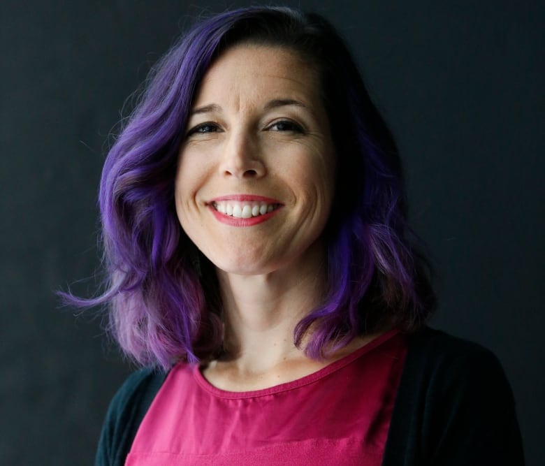 A woman with purple hair and a pink top smiles at the camera.