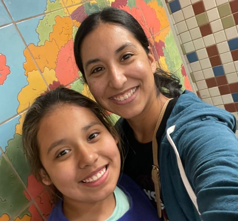 A woman and a young girl, both smiling and wearing their long hair back in ponytails, take a selfie together. 