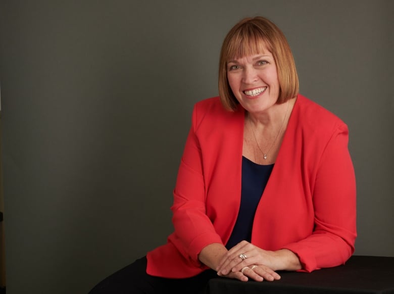 A woman in a red blazer poses for a portrait, hands folds in front of her