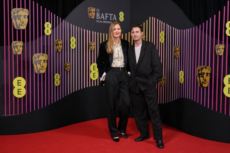 Two people pose for a photograph on a red carpet.