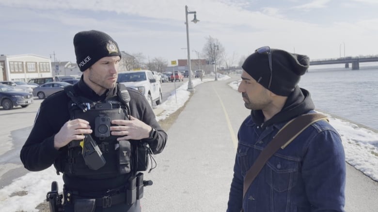 A police officer speaks to a man wearing a toque and jean jacket.