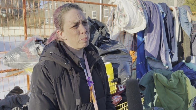 A woman with purple hair and a purple lanyards stands in front of a collection of belongs on top of a fence. 