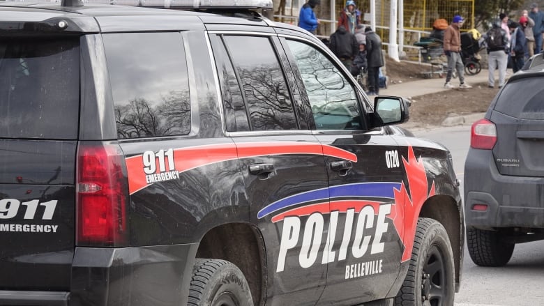 A black parked SUV with a large "Police" sticker on the side. In the background are several people pushing carts of belongings.