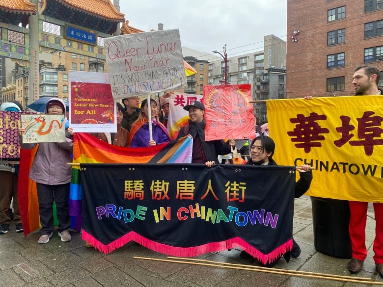 A group of people hold rainbow flags and banners next to a large Chinatown gate, with one of the banners reading 'Pride in Chinatown'.