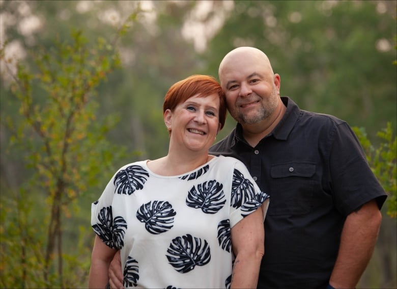 A couple with their heads close together smile at the camera. 