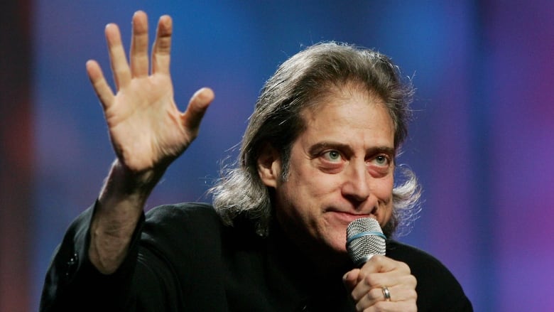 A man holding a microphone to his mouth waves.