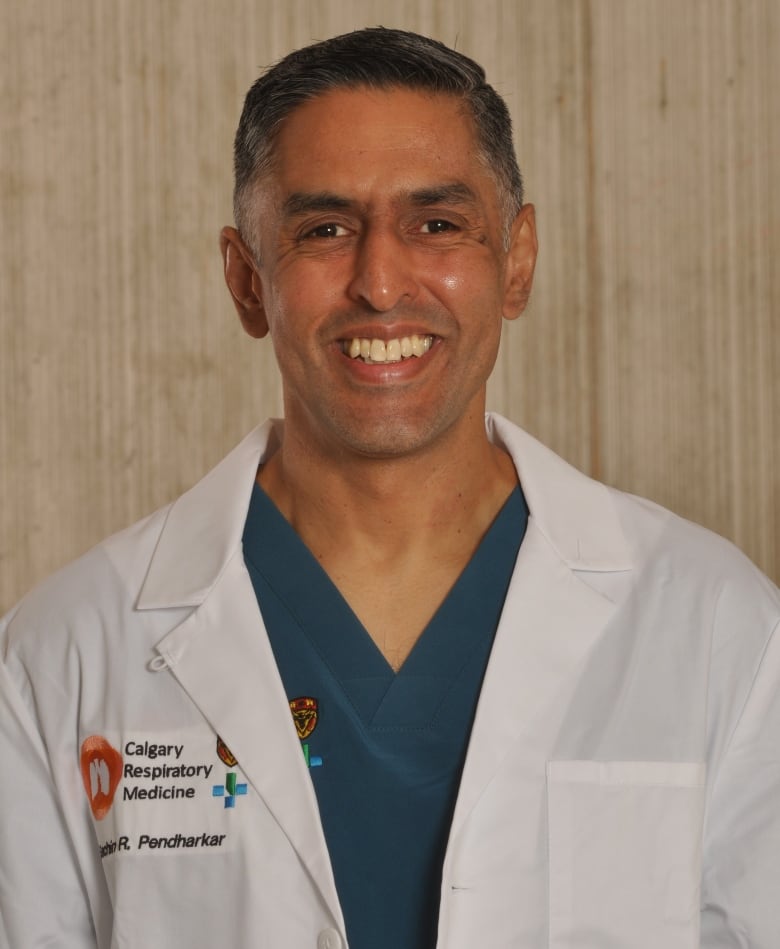 A man in a white lab coat smiles at the camera.