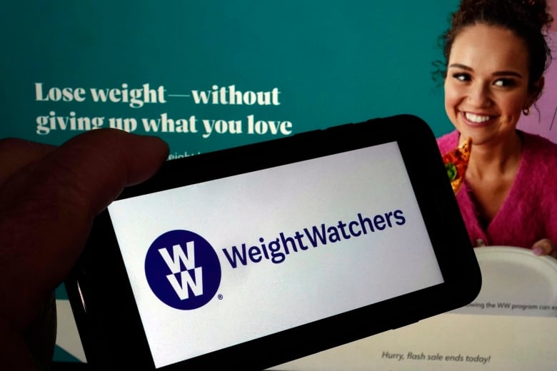 A hand on the lower left corner holds a smartphone horizontally, with the "WeightWatchers" logo in blue on a white screen.