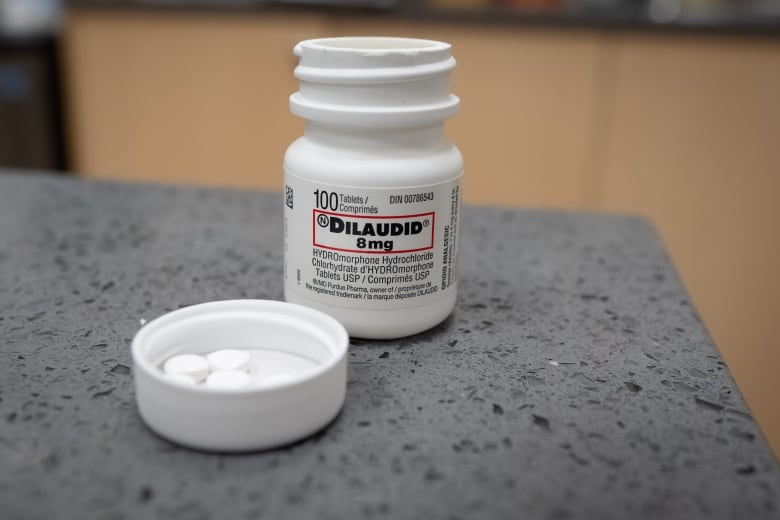 A bottle labeled dilaudid, a pharmaceutically made version of hydromorphone, is open with white pills in the lid, on a counter.