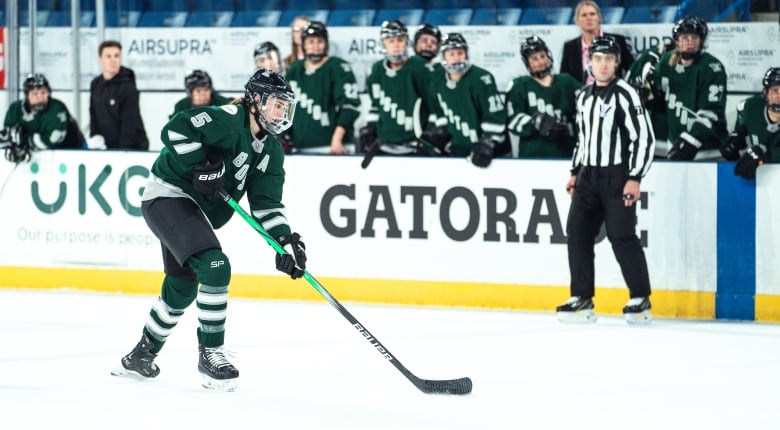 A hockey player in a dark green jersey, with Boston written on it and the number five on the sleeve, carries the puck on the ice.