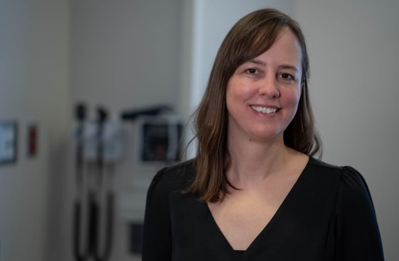 A female doctor with long, brown hair standing in a medical office. 