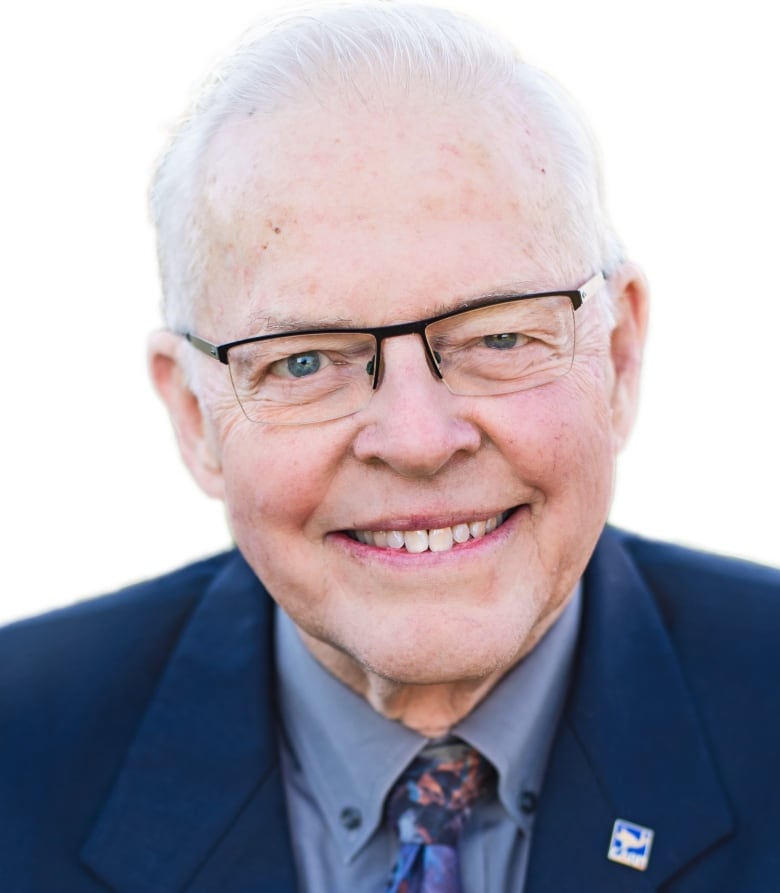 An older man wearing glasses smiles at the camera.