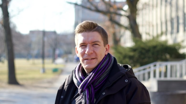 A portrait of a person in a scarf stands in a yard outside.