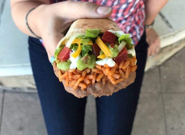 woman's hand holding taco bell's 7-layer burrito