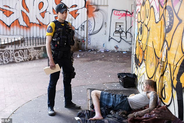 Oregon has seen a 210 per cent increase in fentanyl -related deaths since the initial decriminalization bill was passed in November 2020  (Pictured: Officer Donny Mathew of the Portland Police Bureau's bike squad, stands next to a person who appears to be passed out)