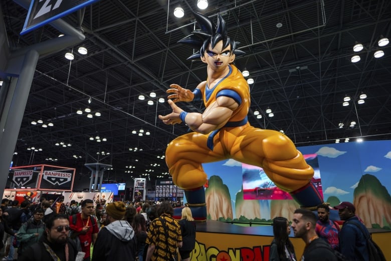 People walk around at what appears to be a convention or event with a massive model of a comic book character shown.