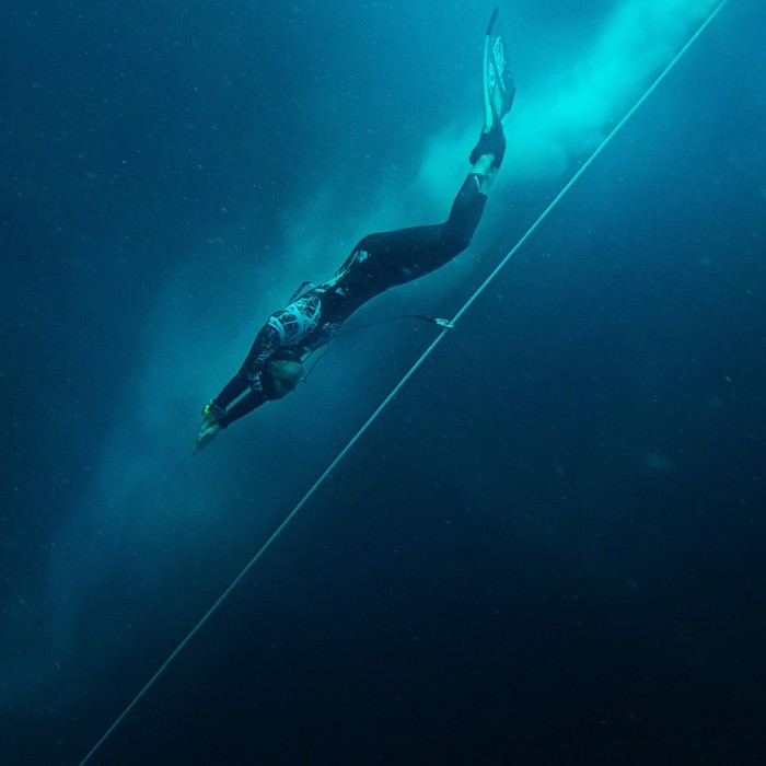 A female freediver in wetsuit and flippers swims downwards 