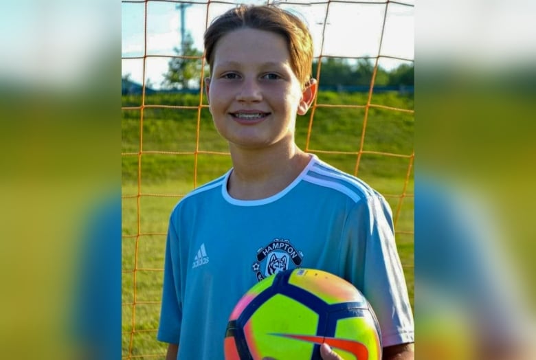 Boy smiling, showing braces on his teeth, holding a brightly coloured soccer ball.