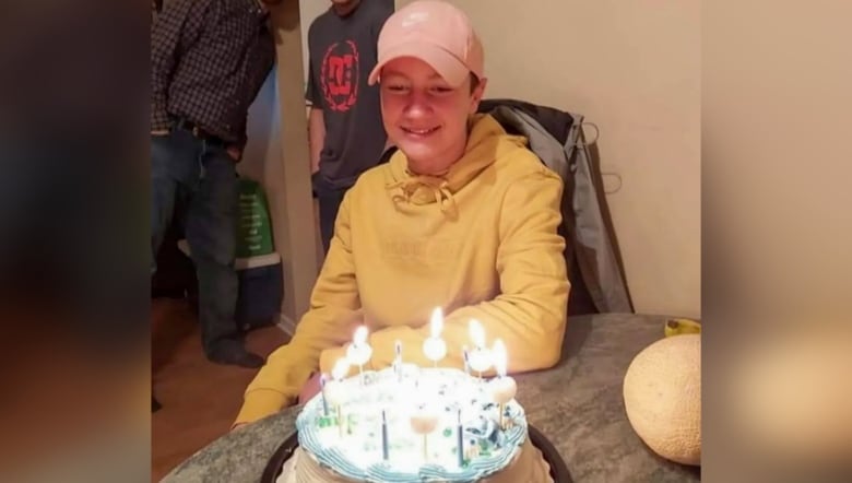 Teenager wearing a hat looking at a birthday cake with candles lit. 