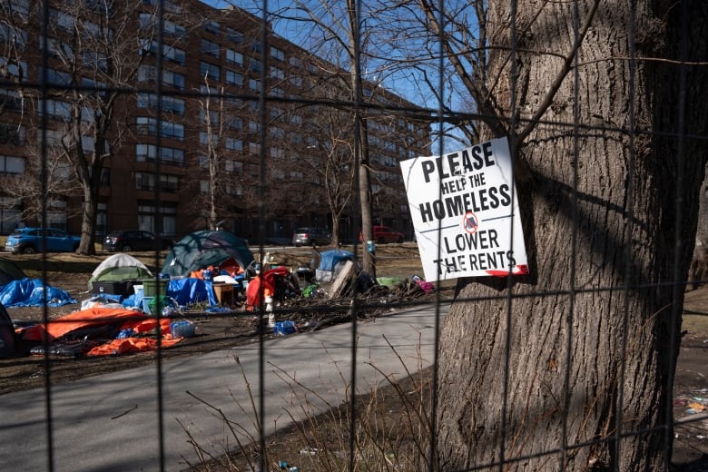 A sign advocating for support for the homeless is seen through a fenced-in homeless encampment in Victoria Park in Halifax's downtown on Monday, March 4, 2024. A fence was erected around the perimeter of the park Monday morning as officials began working with the few remaining residents to leave the de-designated encampment site.