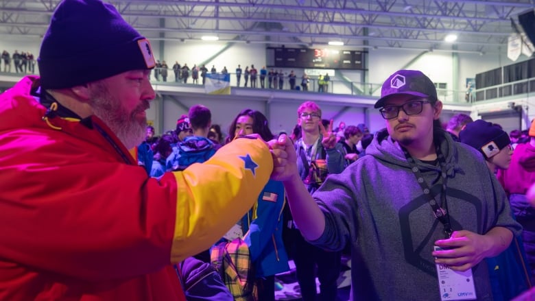 Two people fist bump while someone does bunny ears in background