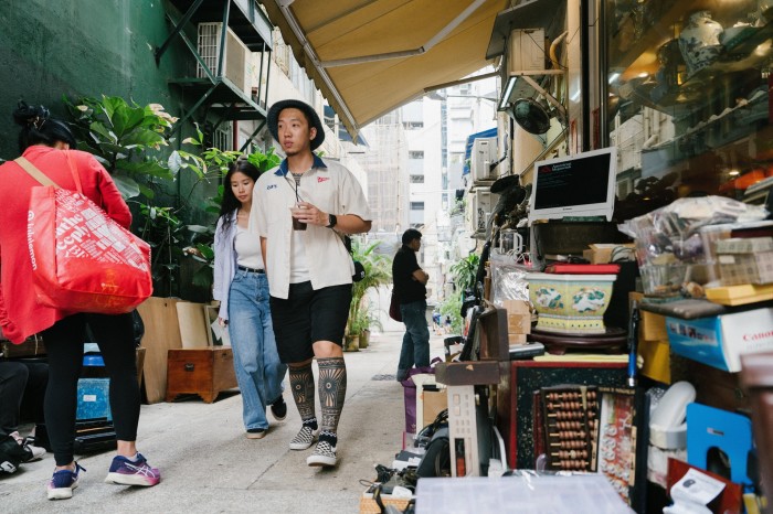 Cool younger people walk past an overflowing antiques/junk shop