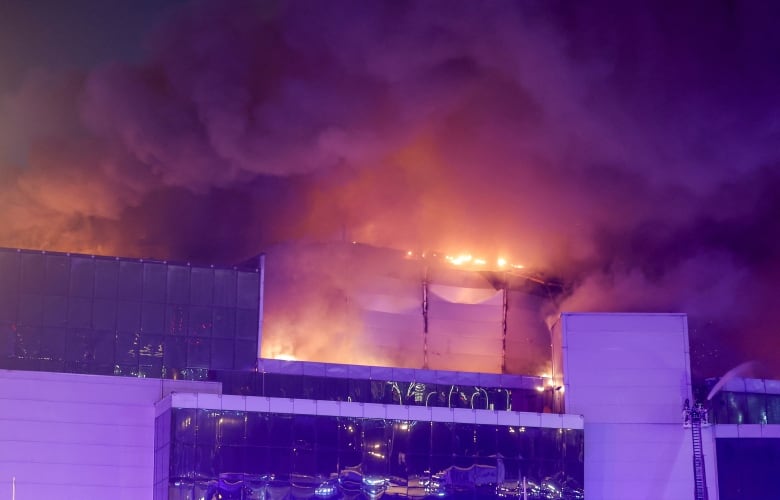 Thick smoke and flames rising out of the top of a large building at night. 