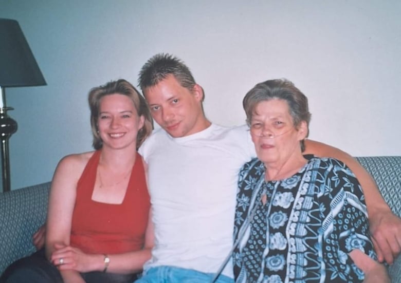 A young woman and man sit on a couch with an older woman. 