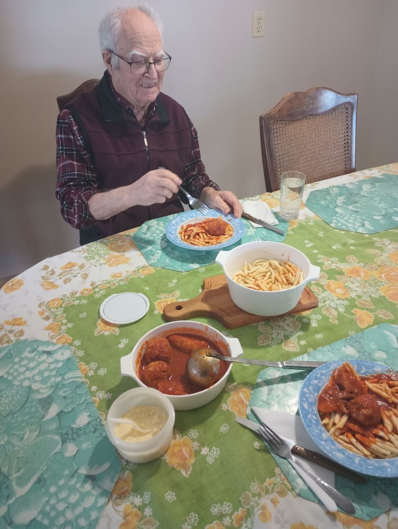 An elderly man eating a pasta lunch. 